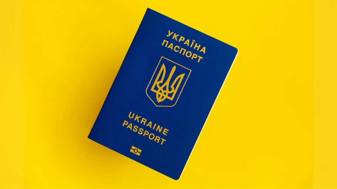 Paszport Ukrainy z niebieską okładką i złotym godłem, leżący na żółtym tle
